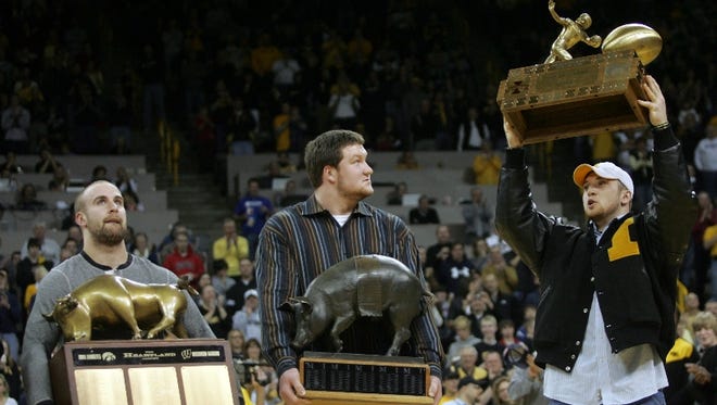 Iowa football players Tyler Sash, left, Bryan Bulaga, center, and Pat Angerer show off the Heartland, Floyd of Rosedale and Cy-Hawk trophies, respectively, as the team is honored in a halftime ceremony during Iowa's men's basketball game against Drake on Saturday night, Dec. 19, 2009, at Carver-Hawkeye Arena in Iowa City.