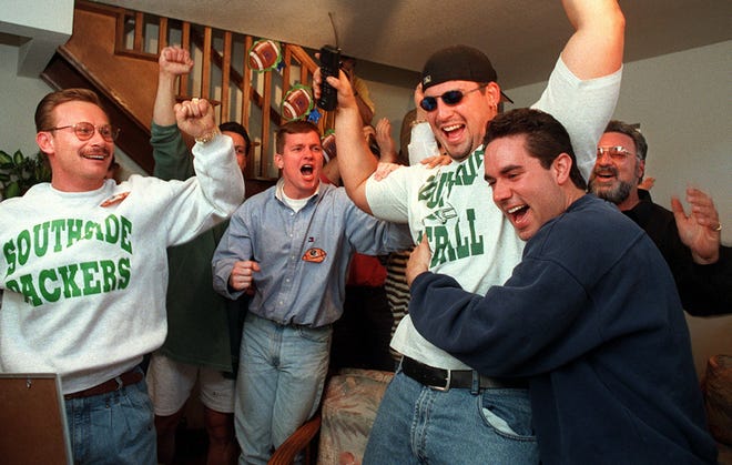 Ross Verba, phone in hand, celebrates with dozens of friends and family as news of his selection in the 1997 NFL Draft was announced on TV. Verba, a former Iowa Hawkeye, was taken 30th ovearll by the Green Bay Packers. He was hugged by his cousin, John Fucaloro. On his left is cousin Steve Fucaloro.