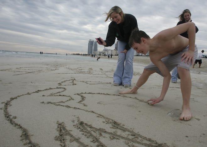 Philip Waddell, 13,of Cedar Rapids, carves a tigerhawk into the sand as his sisters Kayla Waddell, 16, left, and Heather Waddell, right watch, Sunday, Jan. 3, 2010, on South Beach, in Miami Beach, Fl.