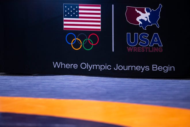 A banner on a table displays the logos of the International Olympic Committee and USA Wrestling, "Where Olympic Journeys Begin," during the USA Wrestling Senior National Championships, Friday, Oct. 9, 2020, at the Xtream Arena in Coralville, Iowa.