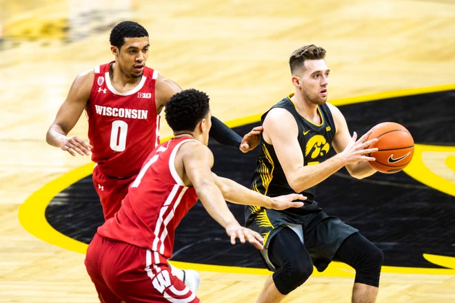 Iowa guard Jordan Bohannon, right, passes as Wisconsin guard D'Mitrik Trice (0) and Wisconsin guard Jonathan Davis (1) defend during a NCAA Big Ten Conference men's basketball game, Sunday, March 7, 2021, at Carver-Hawkeye Arena in Iowa City, Iowa.