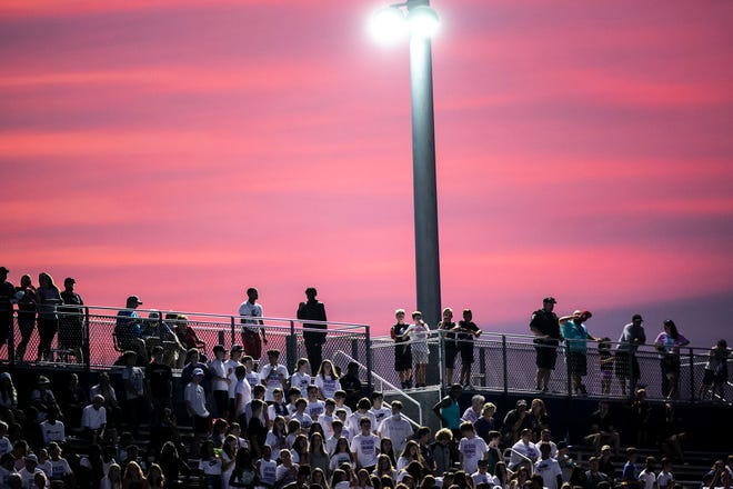 Fans sit in the bleachers as the sun sets behind them during a varsity high school football game, Friday, Aug. 27, 2021, at Liberty High School in North Liberty, Iowa.