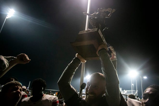 Iowa City High head coach Mitchell Moore lifts the Titans Trophy while celebrating with players after a varsity high school football game against Iowa City Liberty, Friday, Aug. 27, 2021, at Liberty High School in North Liberty, Iowa. The Little Hawks beat the Lightning, 41-0.